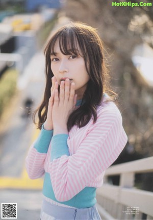 A woman in a pink sweater and white skirt standing on a street.