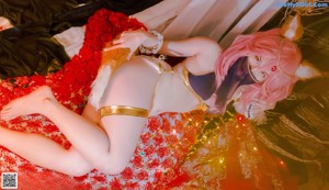 A woman with pink hair sitting on a bed.