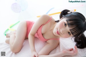 A young girl in a pink leotard sitting on a pink rug.
