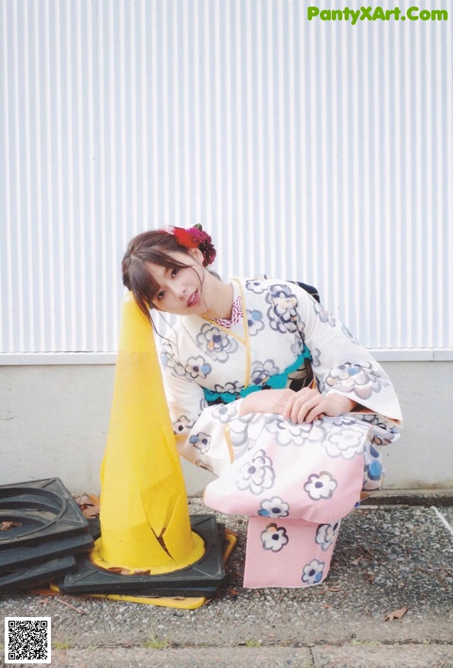 A woman in a kimono sitting on the ground next to a traffic cone.