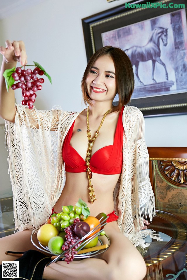 A woman in a red bikini holding a bunch of grapes.