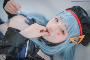 A woman with blue hair sitting on a bathtub holding a book.