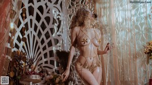 A woman in a gold bodysuit standing in front of a curtain.