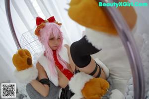 A woman with pink hair sitting in a ball pit holding a teddy bear.