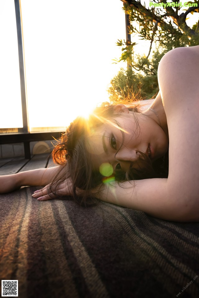A woman laying on the ground with the sun setting behind her.
