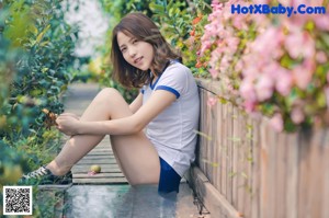 A woman sitting on a wooden bench next to a bush.