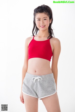 A woman in a red top and gray shorts standing on a white surface.