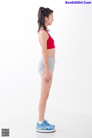 A woman in a red top and gray shorts leaning against a wall.