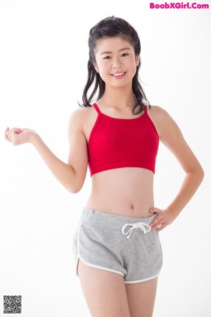 A woman in a red top and gray shorts holding a red resistance band.