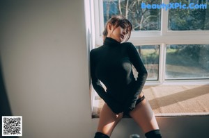 A woman in a black bodysuit posing in front of a window.