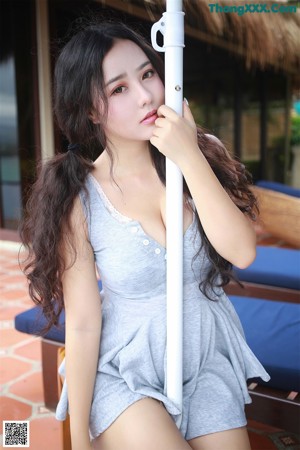 A woman in a gray dress holding a lollipop in her mouth.