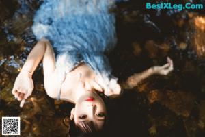 A woman in a blue dress laying on a rock.