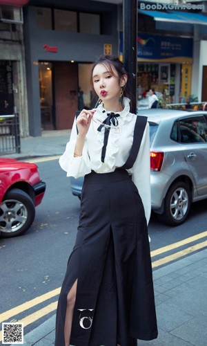 A woman in a white shirt and black pants leaning against a pole.