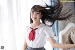 A woman in a school uniform standing in front of a bed.