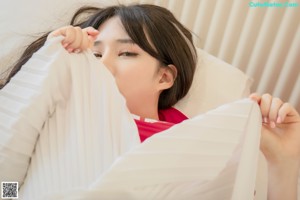 A woman in a red top and white skirt laying on a bed.