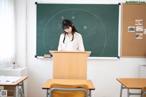 A woman sitting at a desk in front of a blackboard.