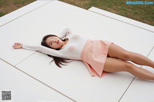 A woman in a white shirt is posing naked on a bed.