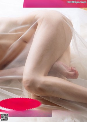 A naked woman sitting on top of a bed covered in a sheet.