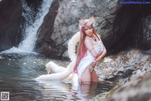 A woman in a white dress sitting on a rock next to a stream.